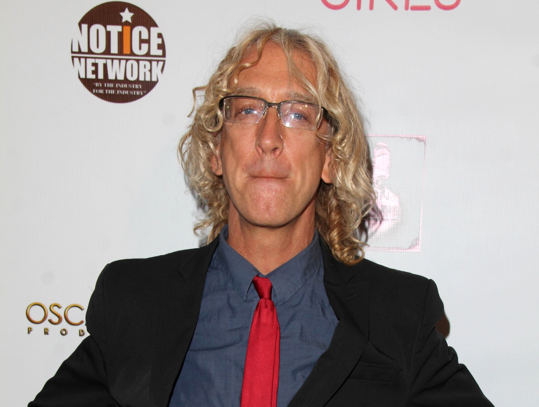 Andy Dick wearing black suit with blue shirt and red tie is looking at camera - 2014