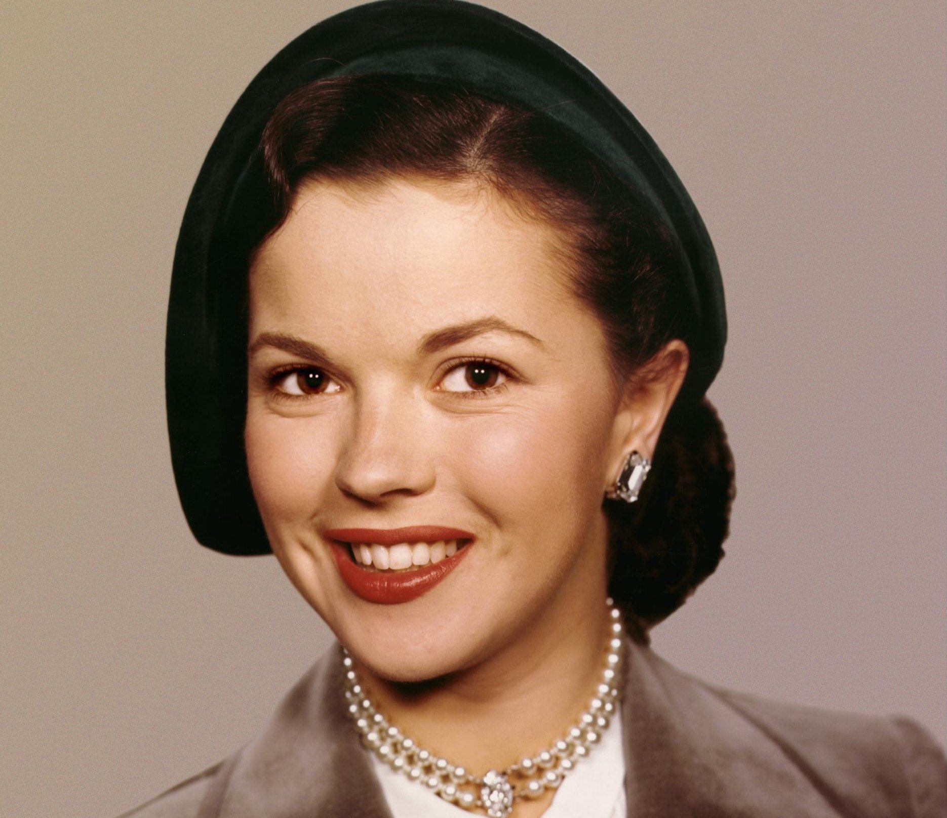 Shirley Temple in brown jacket and hat wearing pearls