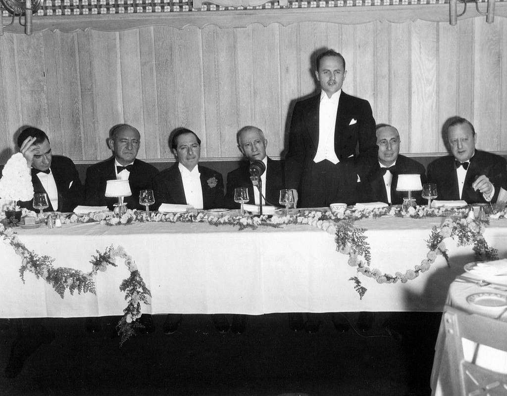 George Jessel at dinner wearing suit sitting on a desk