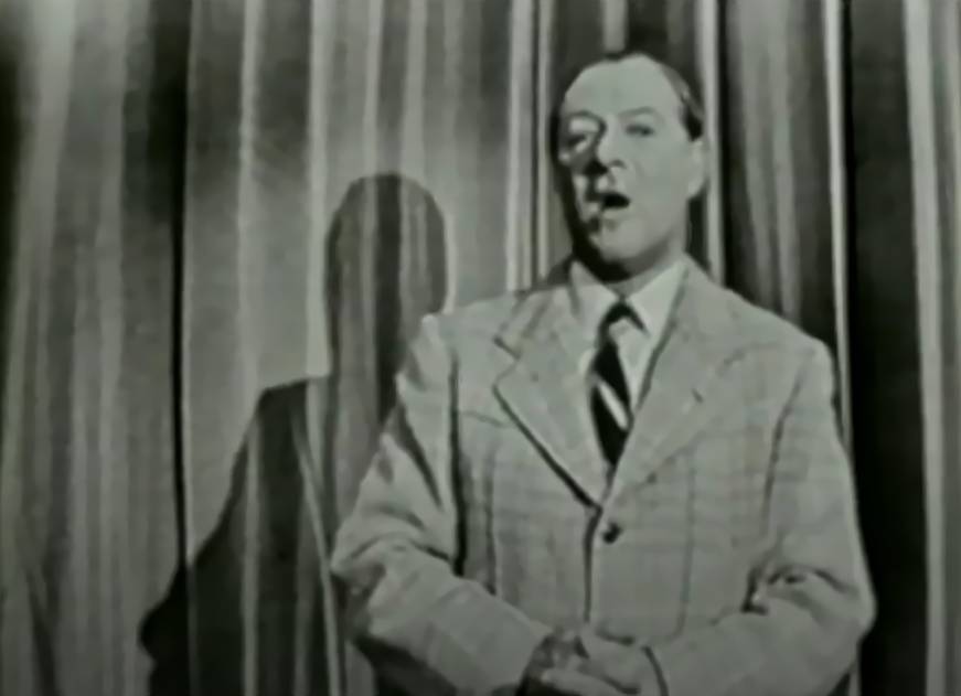 George Jessel in suit speaking in front of a camera