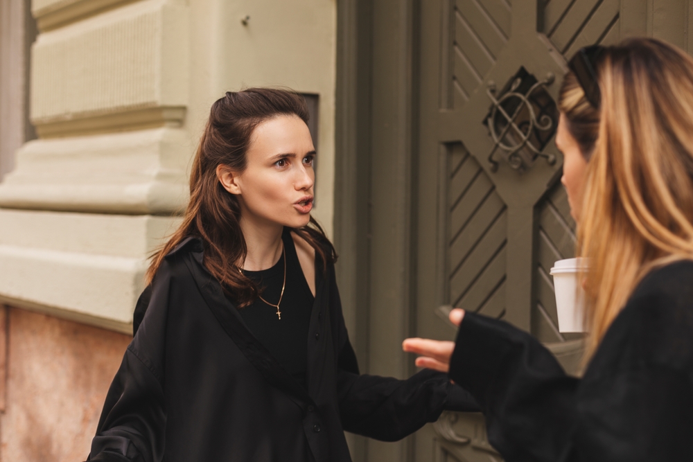 Two young women in black clothes argue near door outdoor