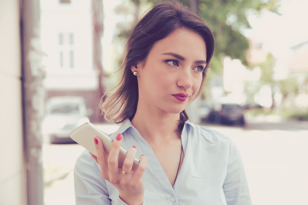 Frustrated annoyed sad woman with mobile phone in blue shirt standing outside in the street