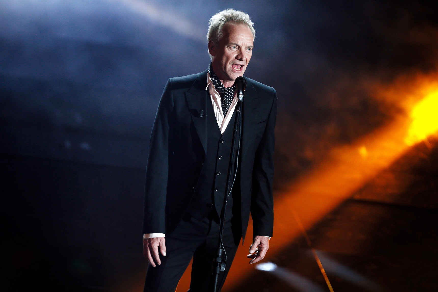 Sting wearing black suit is performing on stage live - 2018