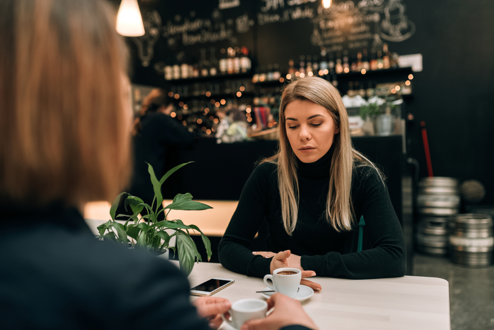 Two girl friends in black clothes at a restaurant having a serious conversation