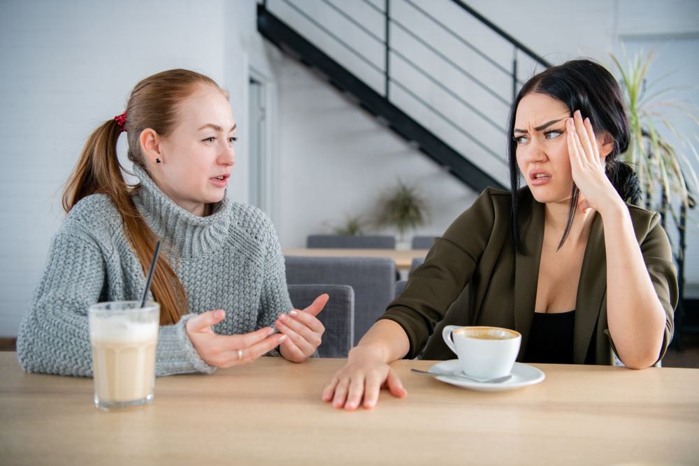 Two young women argue in café sitting at the table