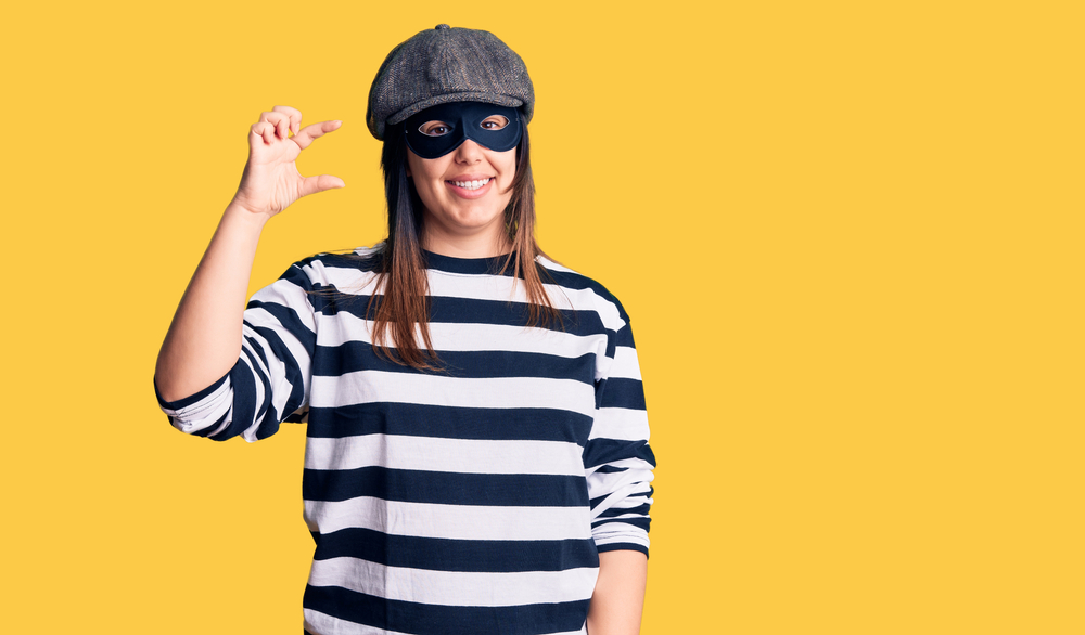 Young beautiful brunette woman wearing burglar mask smiling and confident gesturing with hand doing small size sign with fingers