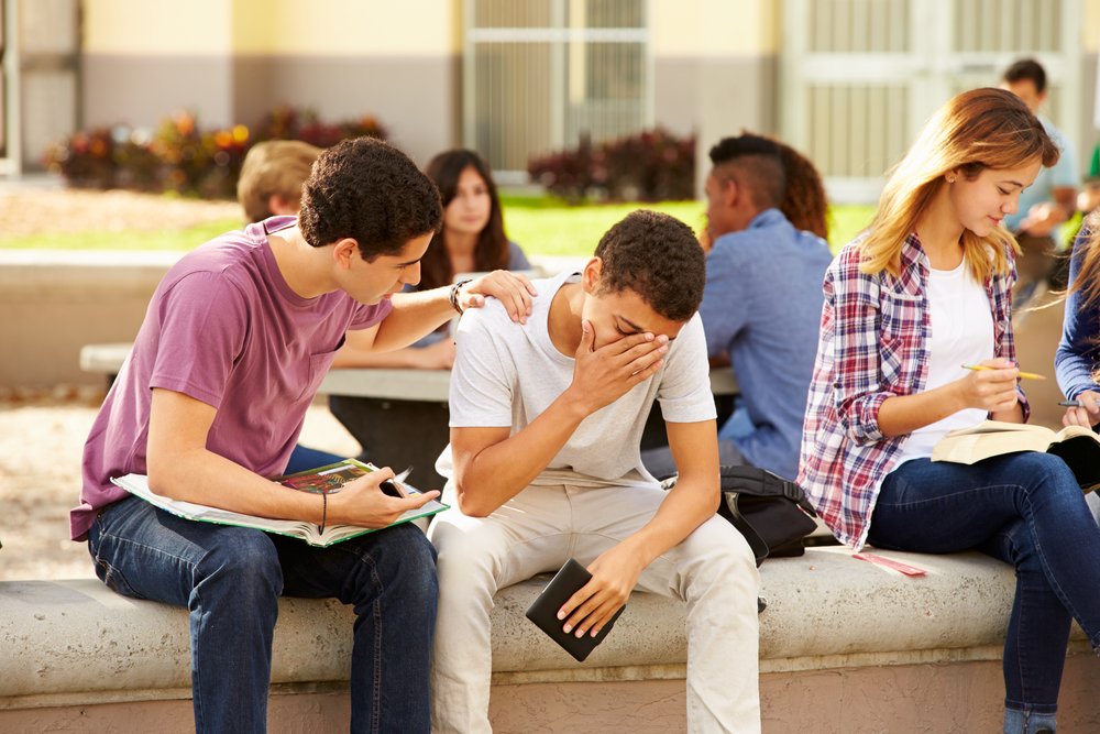 Male High School Student Comforting Unhappy Friend in school yard