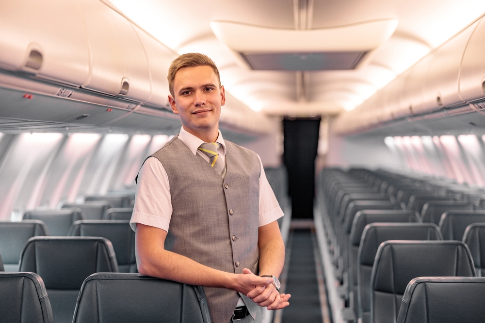Male flight attendant in uniform standing in an empty aircraft passenger salon