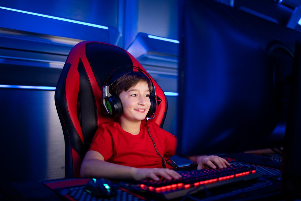 Professional young gamer boy with headphones sitting in comfortable chair