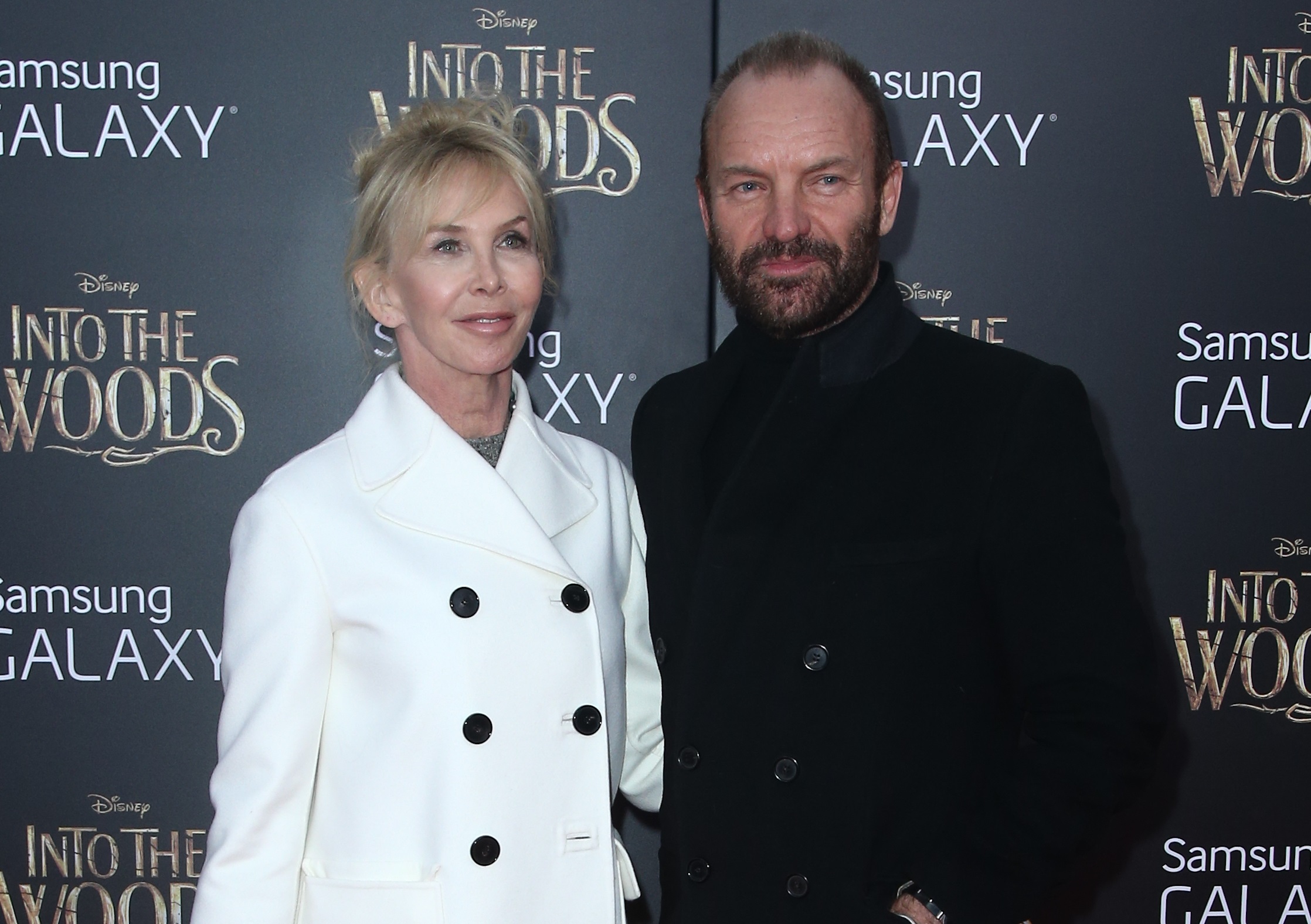 Singer Sting with beard ,wearing black coat (R) and wife Trudie Styler wearing white coat are standing in front of a cameras and smiling - 2014