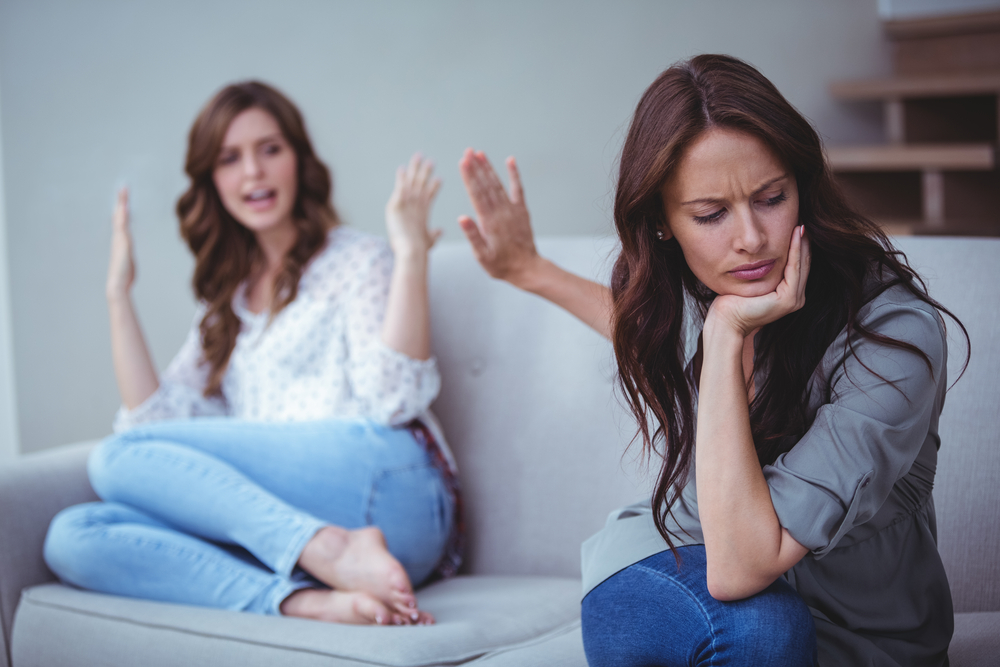 Two female friends sitting on sofa and arguing