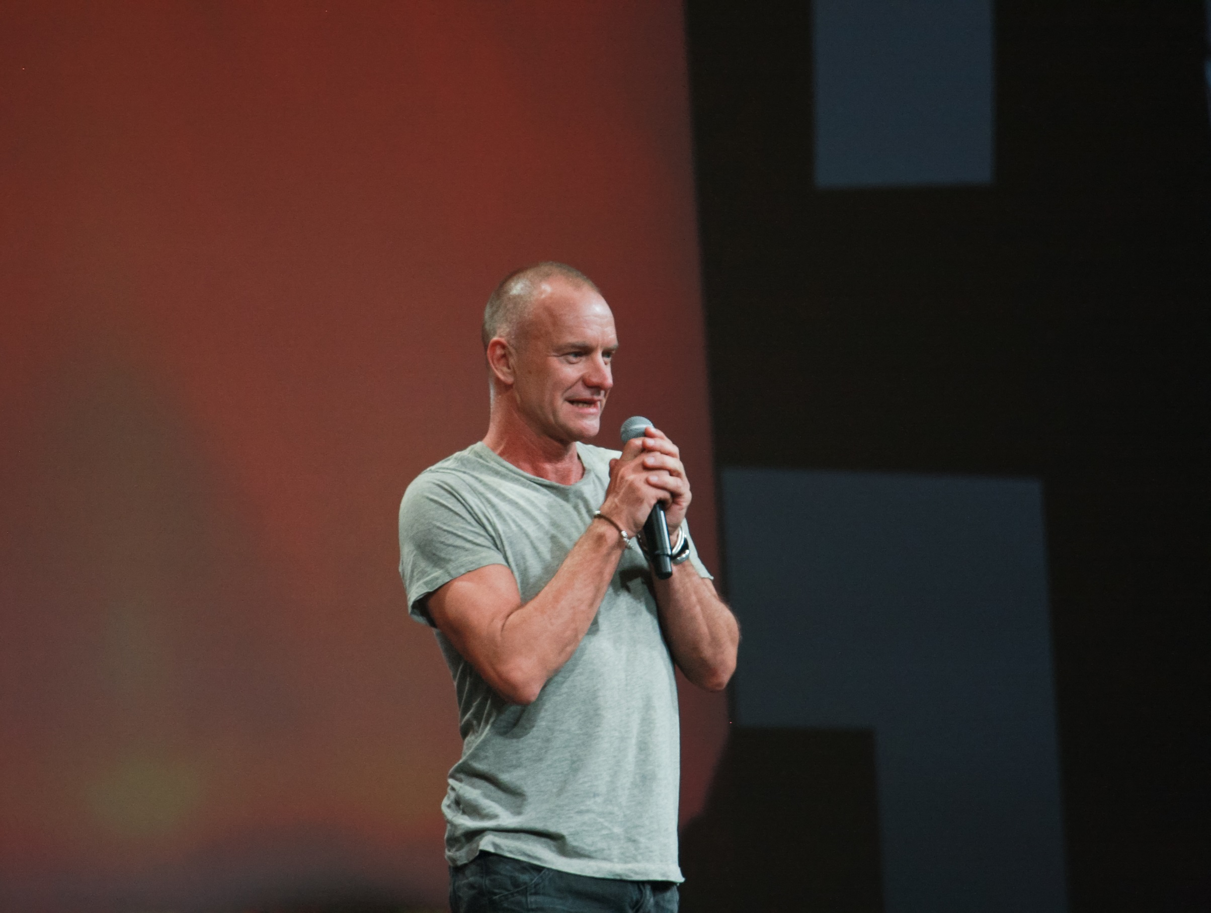 Sting wearing green shirt is smiling and talking to the people on stage - 2011