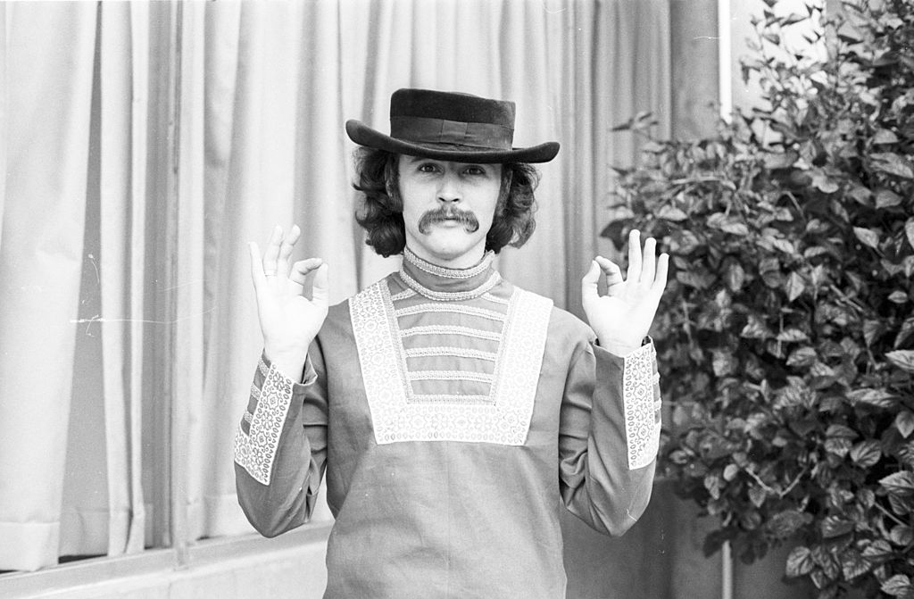 Photo of David Crosby in shirt and a hat with lifted hands