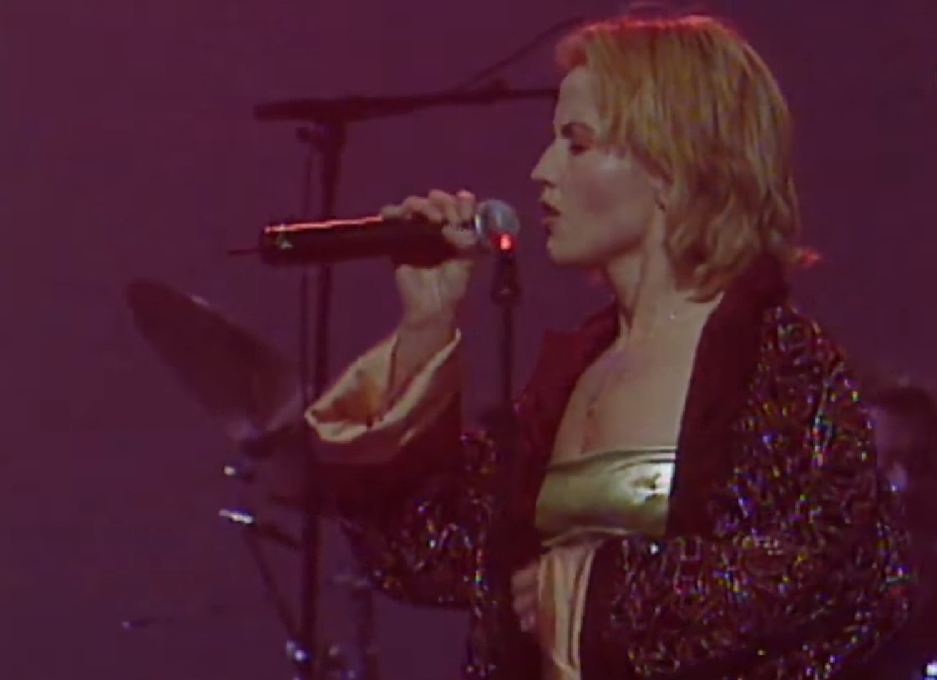 Screenshot: Dolores O'Riordan wearing dark coat is singing live on stage - from Dolores (TV documentary,2018)