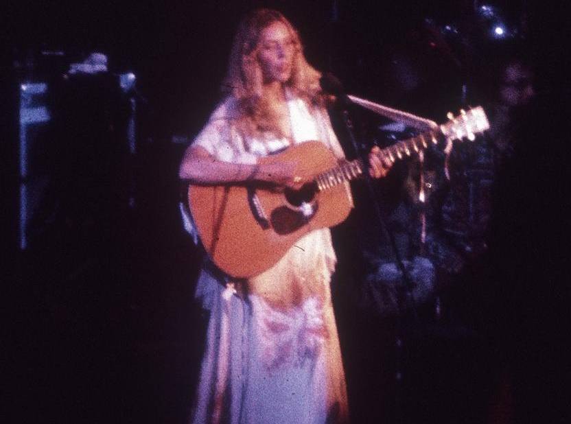 Joni Mitchell performing on stage in white dress