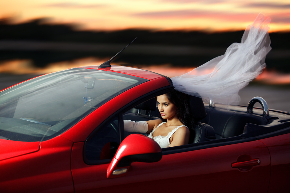 Bride running away in red cabriolet in her wedding dress