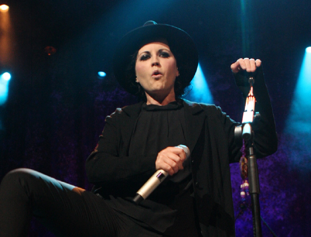 Dolores O'Riordan wearing black hat is performing on stage - 2012
