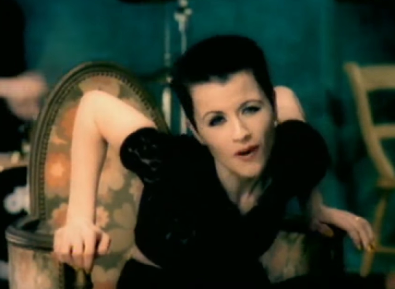 Screenshot: Dolores O'Riordan seating on chair and singing - from Dolores (TV documentary,2018)