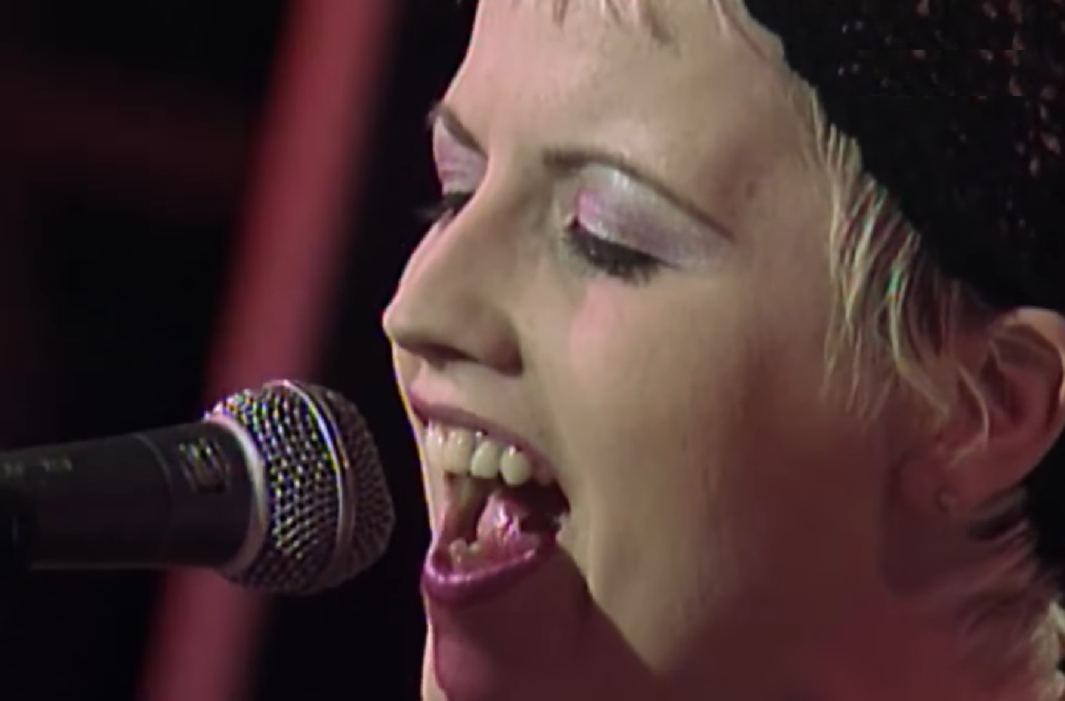 Screenshot: Dolores O'Riordan wearing black hat is performing on stage - from Dolores (TV documentary,2018)