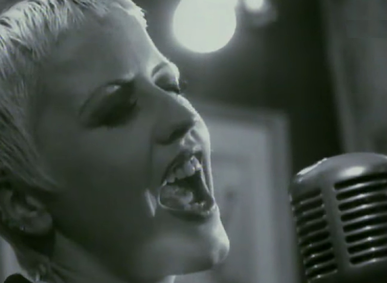 B&W Screenshot: Dolores O'Riordan is singing on a microphone (close up) - from Dolores (TV documentary,2018)
