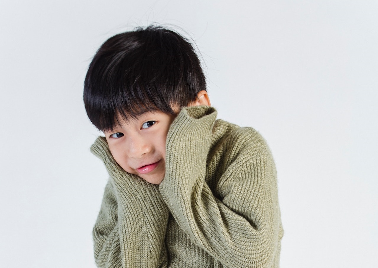 Cute boy wearing green sweater with shy face is looking at camera.