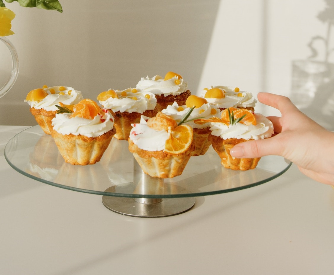 A person is hand holding a cupcake with cream from a glass trey.
