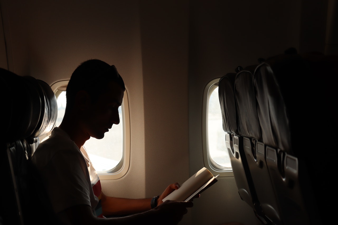 Man is reading a book on airplane.