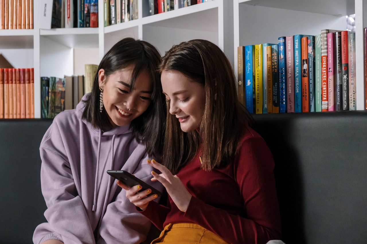 A girl in red sweater holding her phone while talking to her friend.