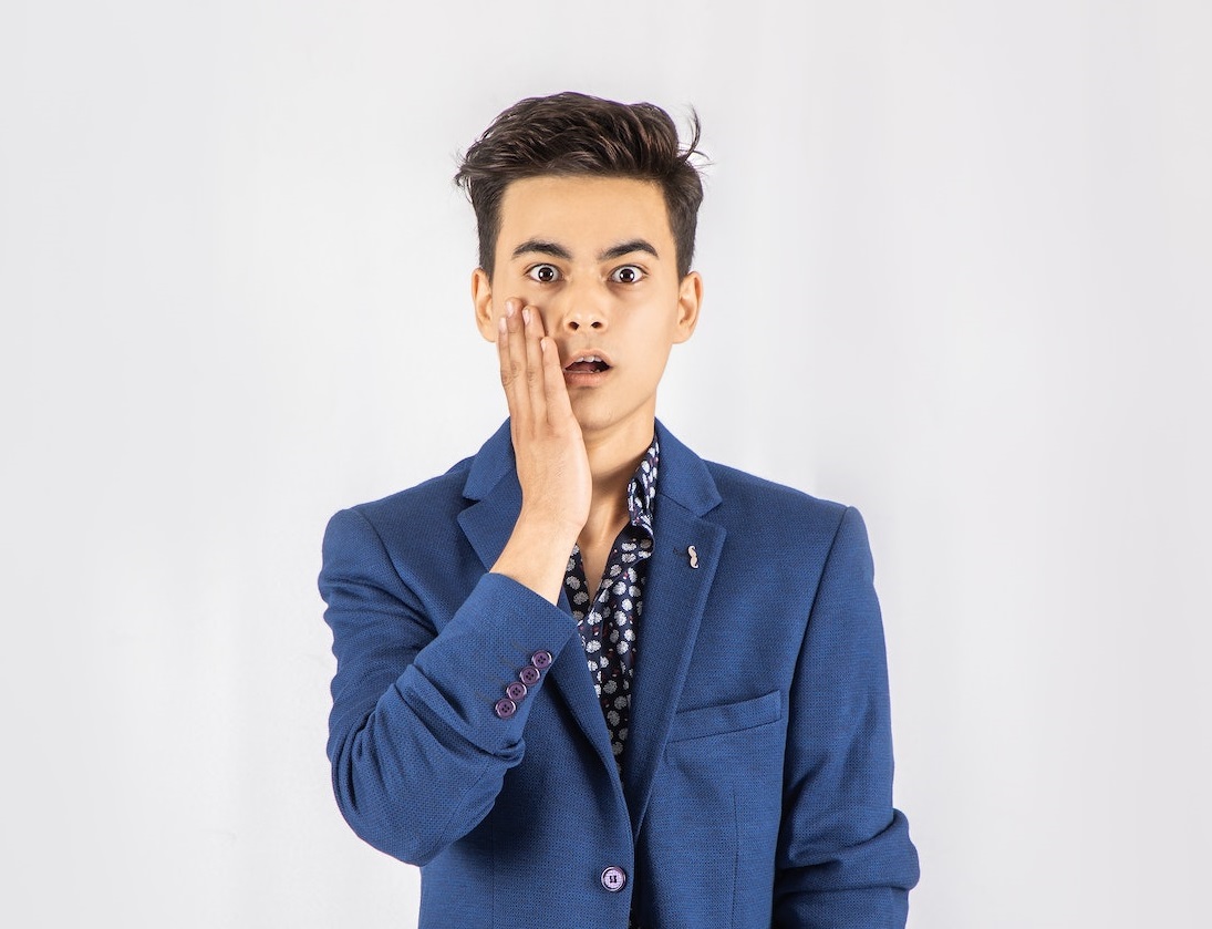 Shocked man in blue jacket standing in front of white background.