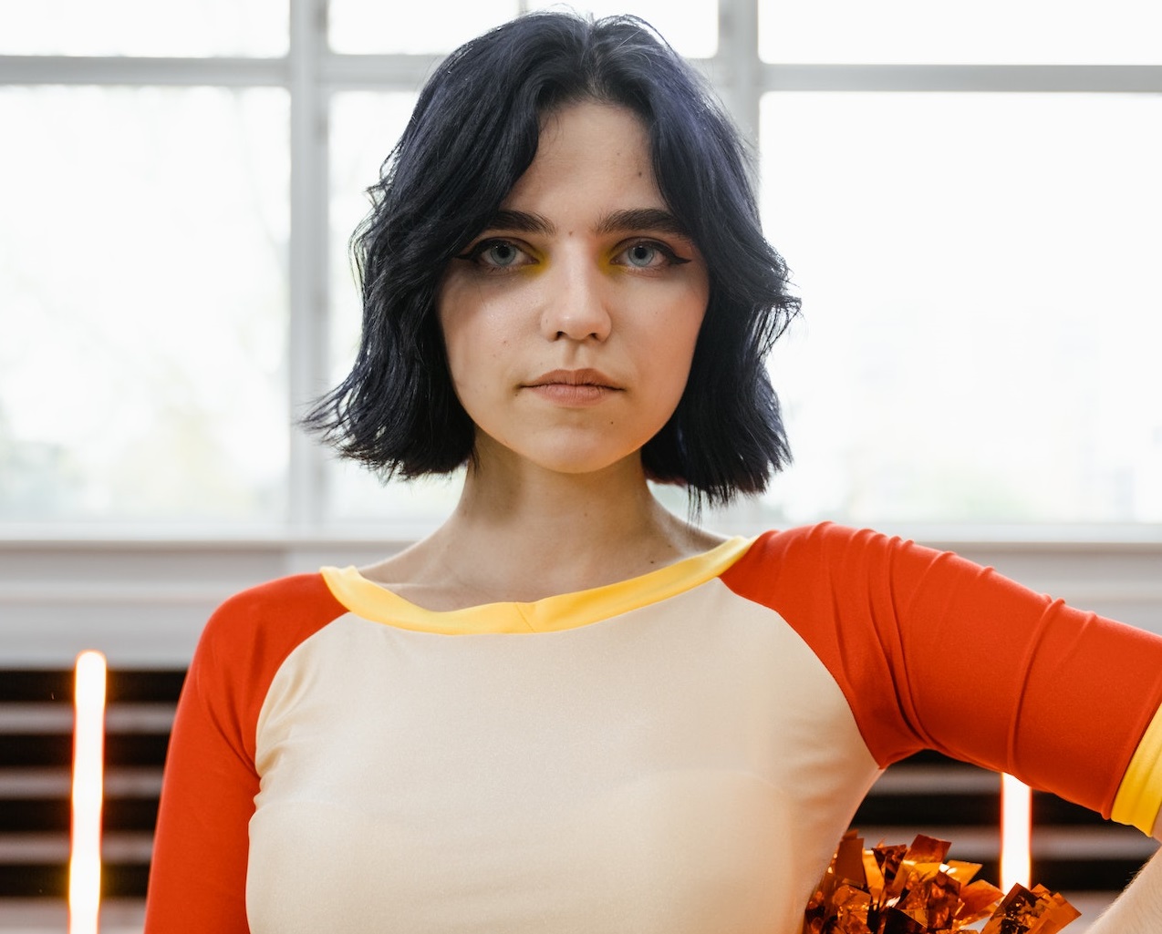 Young woman wearing cheerleader uniform is posing with a pompom on hand.