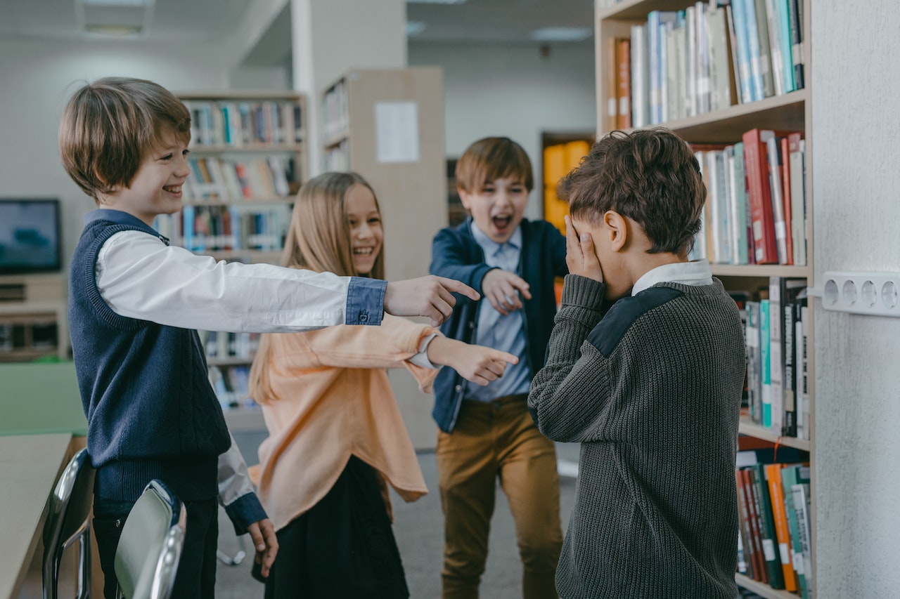 Children laughing and pointing with fingers at a sad boy.