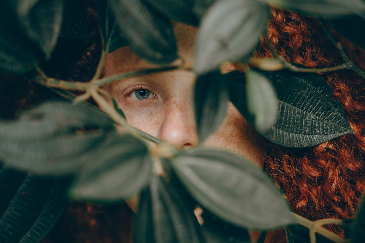 Girl with red hair is hiding behind leaves.