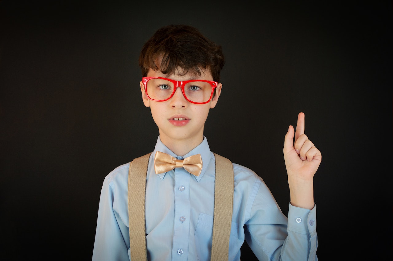 Boy with red glasses is pointing up with his finger.