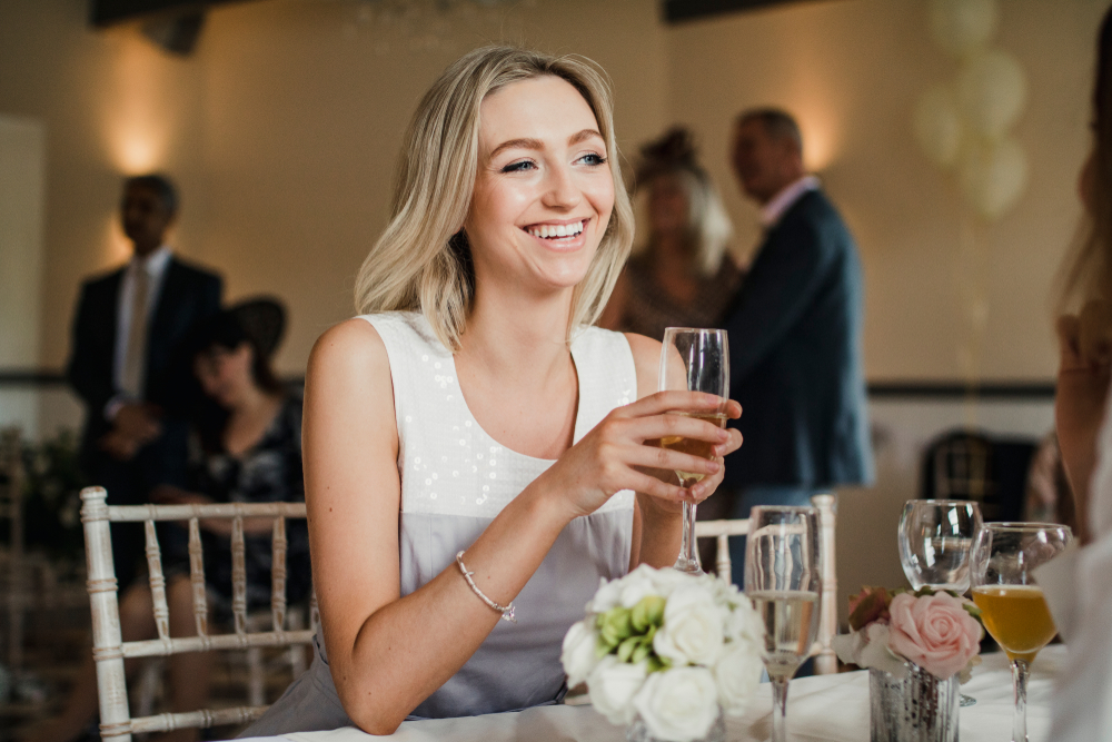 Young woman  sitting at a table at a wedding with a glass of champagne