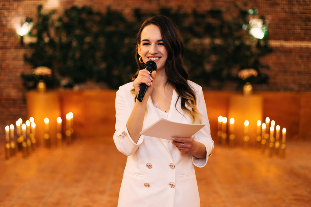 Woman at a wedding  holds microphone to give a  speech in white suit