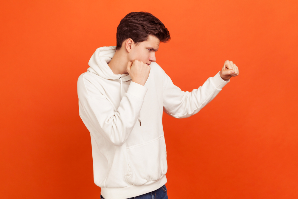 Young man defending from bullies in white sweatshirt with his fists up