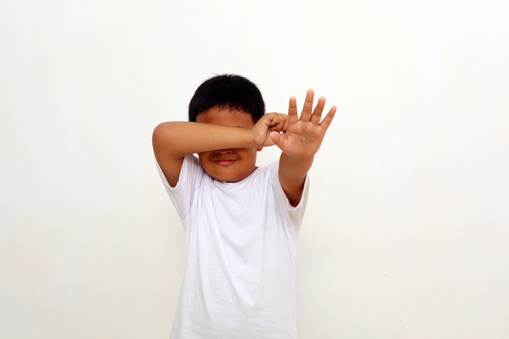 Crying Asian boy standing with stop hand gesture in white t-shirt .