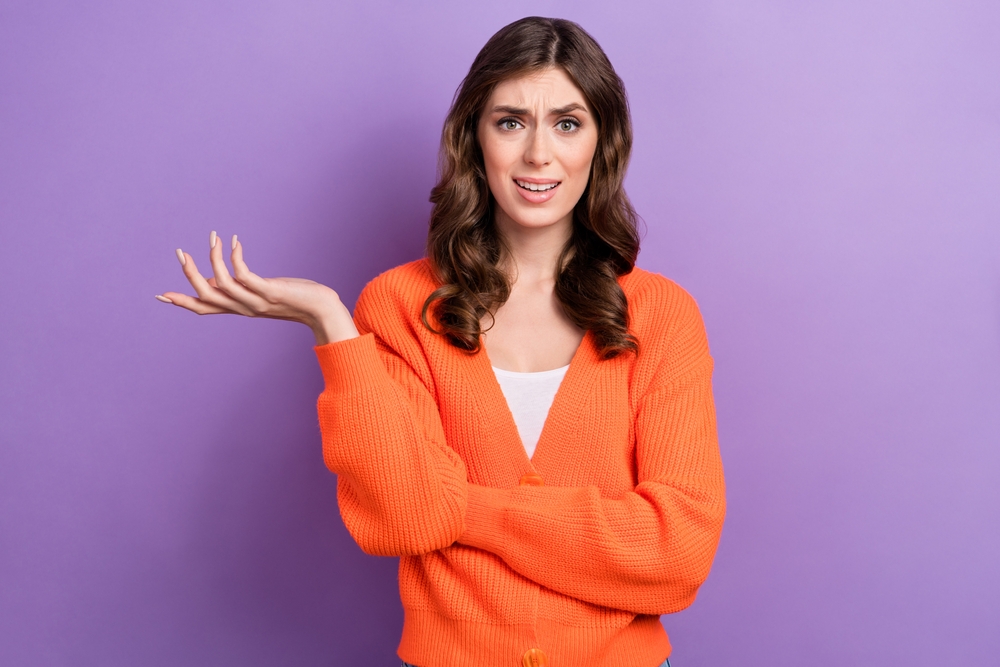 Portrait of unsatisfied woman with  raised arm gesture saying she is mad about something in orange sweater
