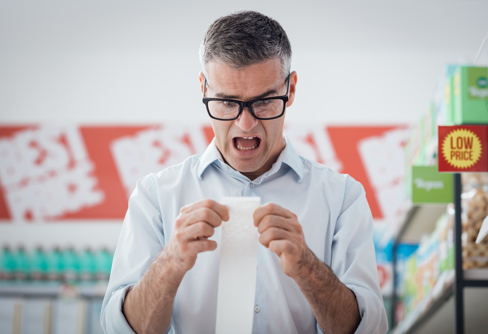 Shocked man doing grocery shopping at the supermarket and checking a long receipt