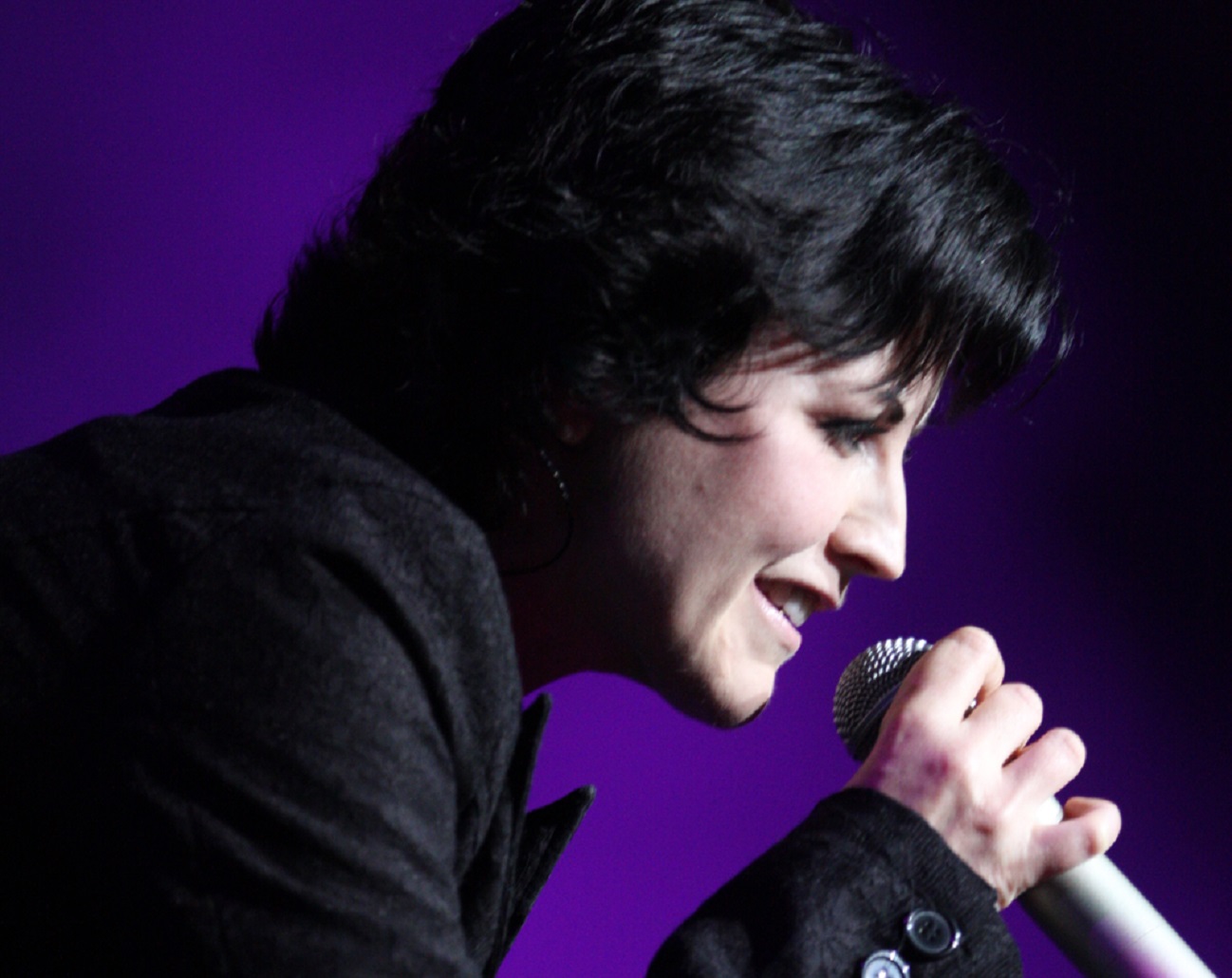 Dolores O'Riordan is singing on a stage in purple background - 2012