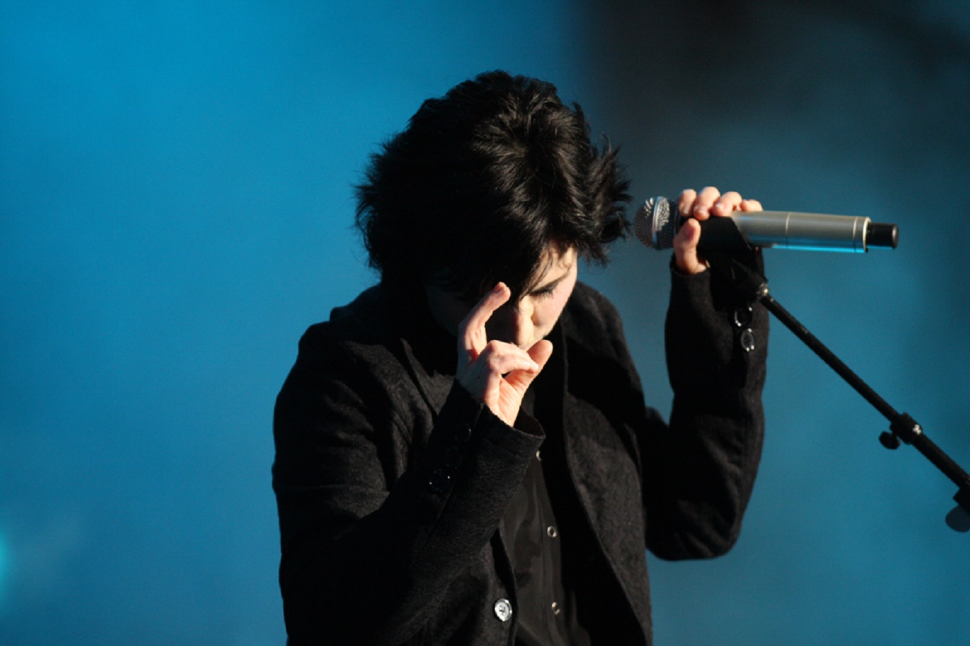 Dolores O'Riordan wearing black suit is singing live on stage on blue background - 2012