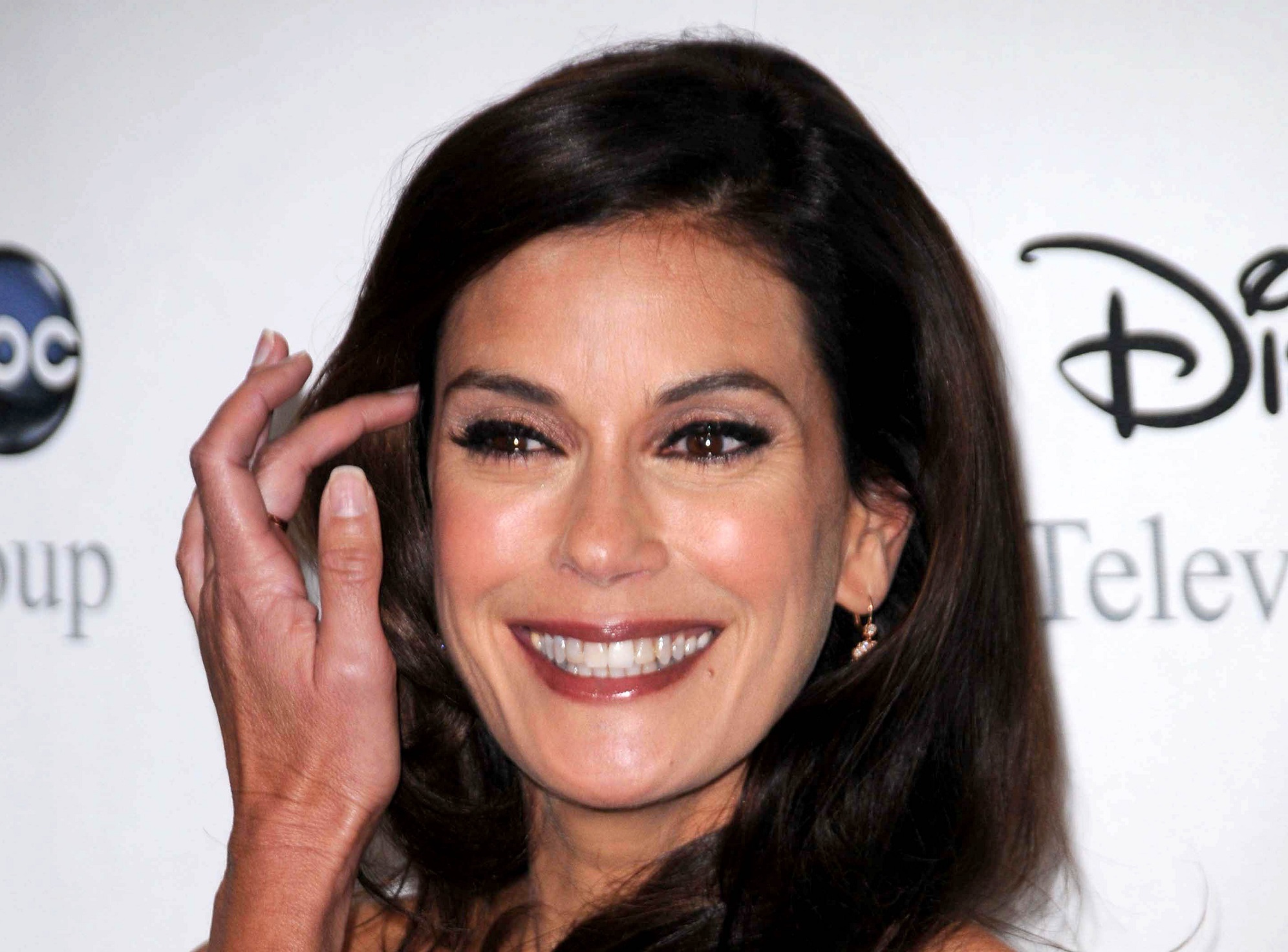 Teri Hatcher wearing red lipstick and earrings is smiling and looking at side,touching her hair - 2008