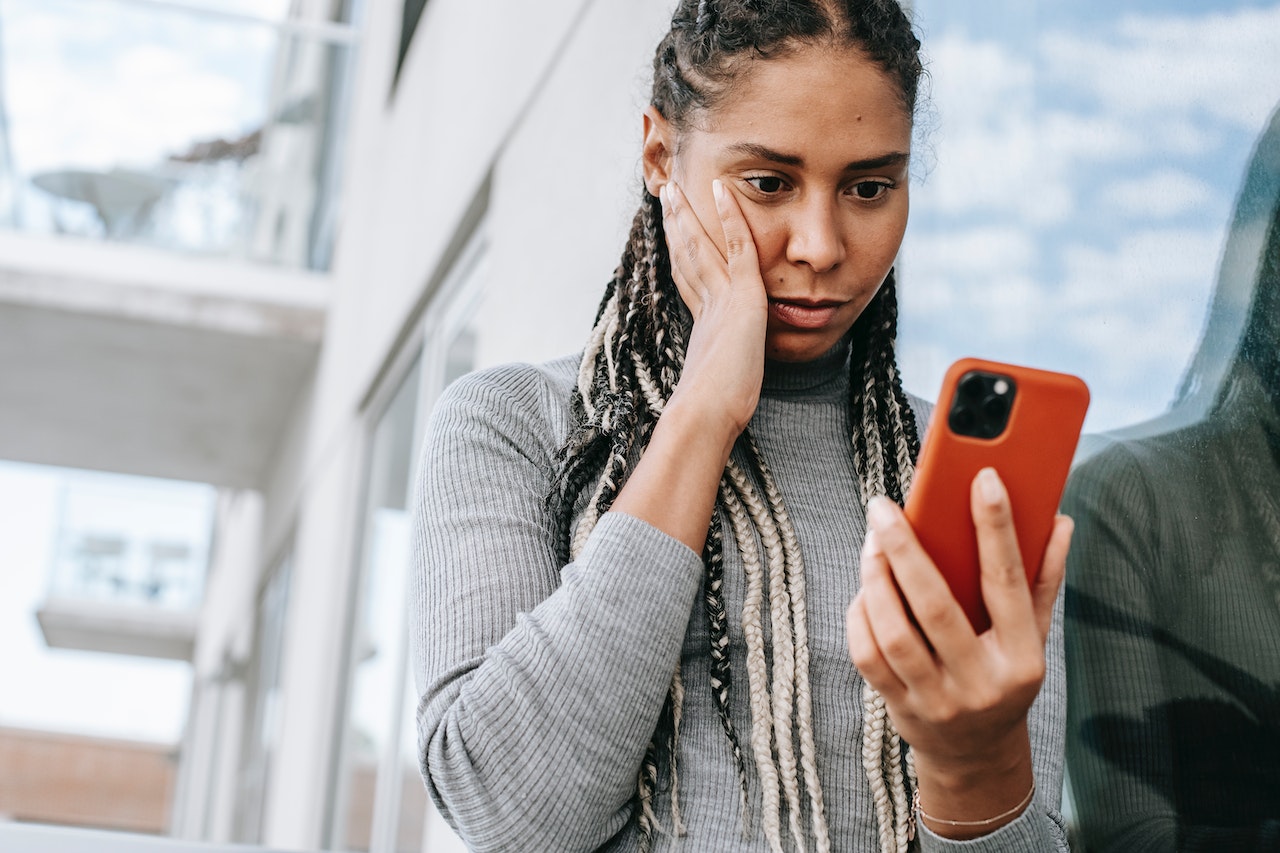 Black woman is reading message on the phone and looking shocked.
