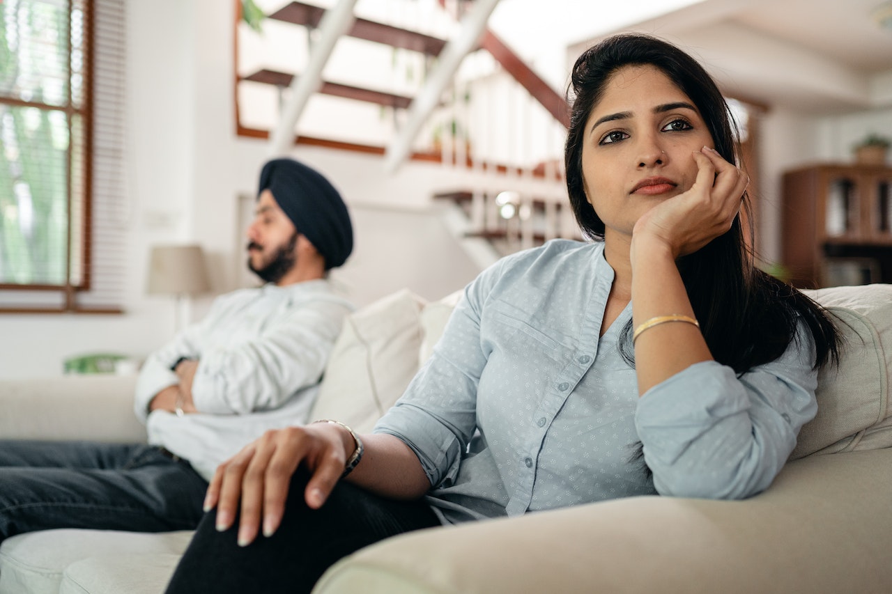 Sad woman avoiding talking to husband while sitting on sofa.