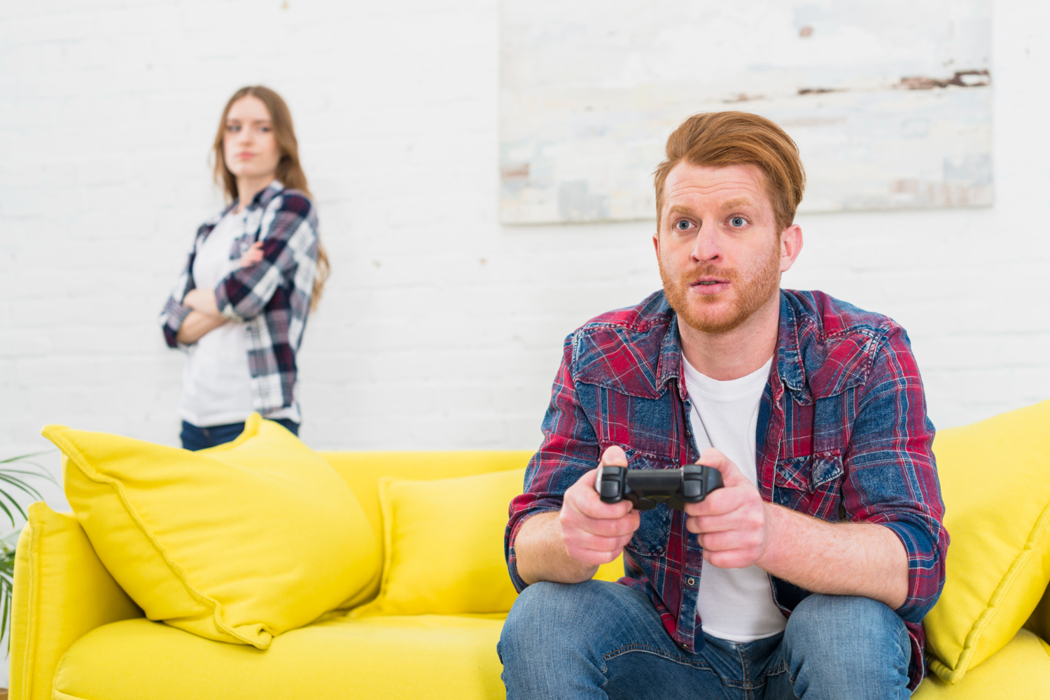 Woman is looking upset at man seating on the sofa and playing PS.