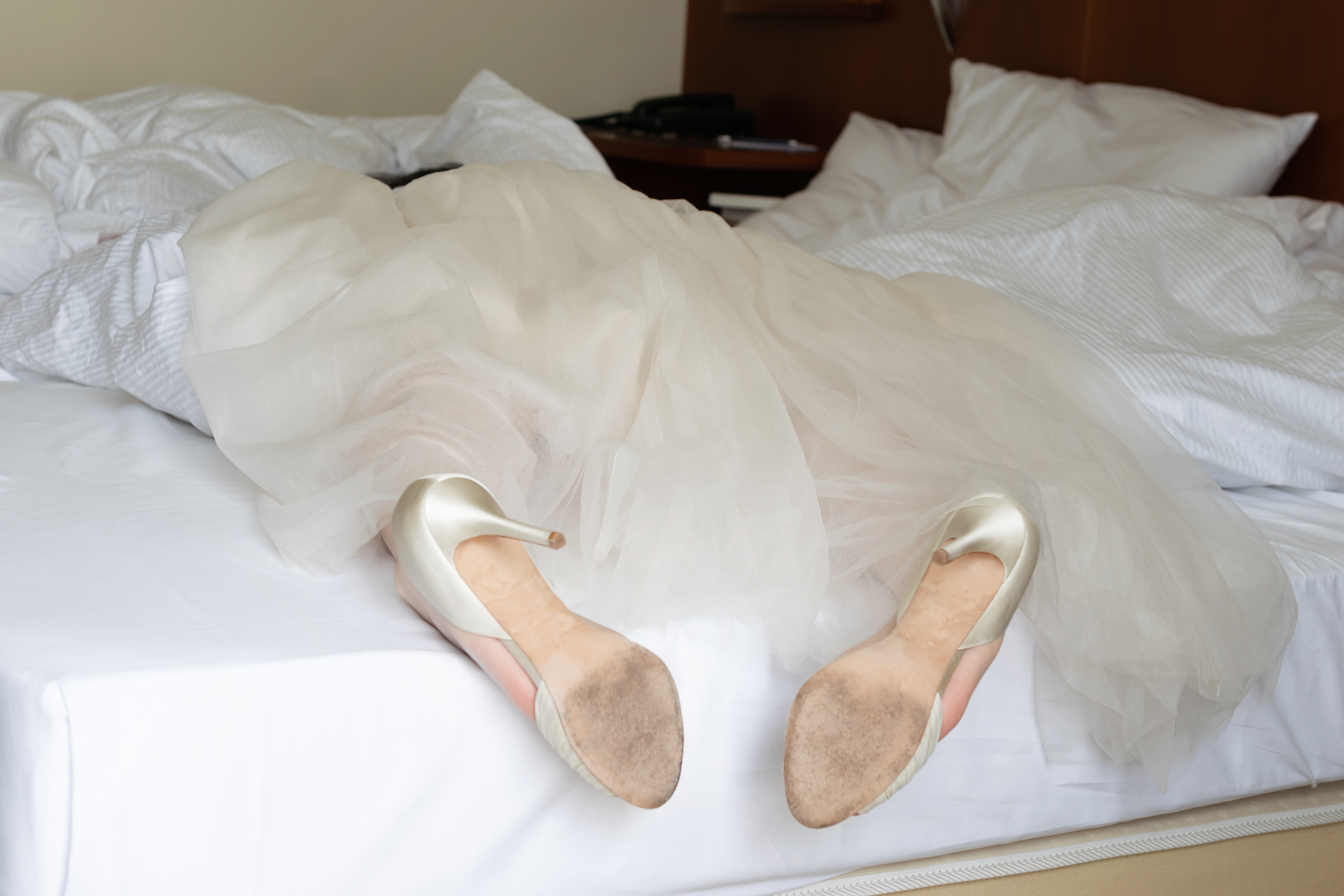 Close up on a drunk bride laying on a bed in her wedding dress and shoes.