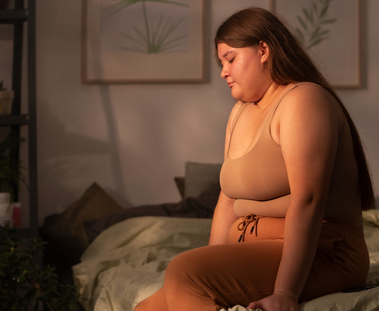 Oversized woman is seating on the bed with sad face.