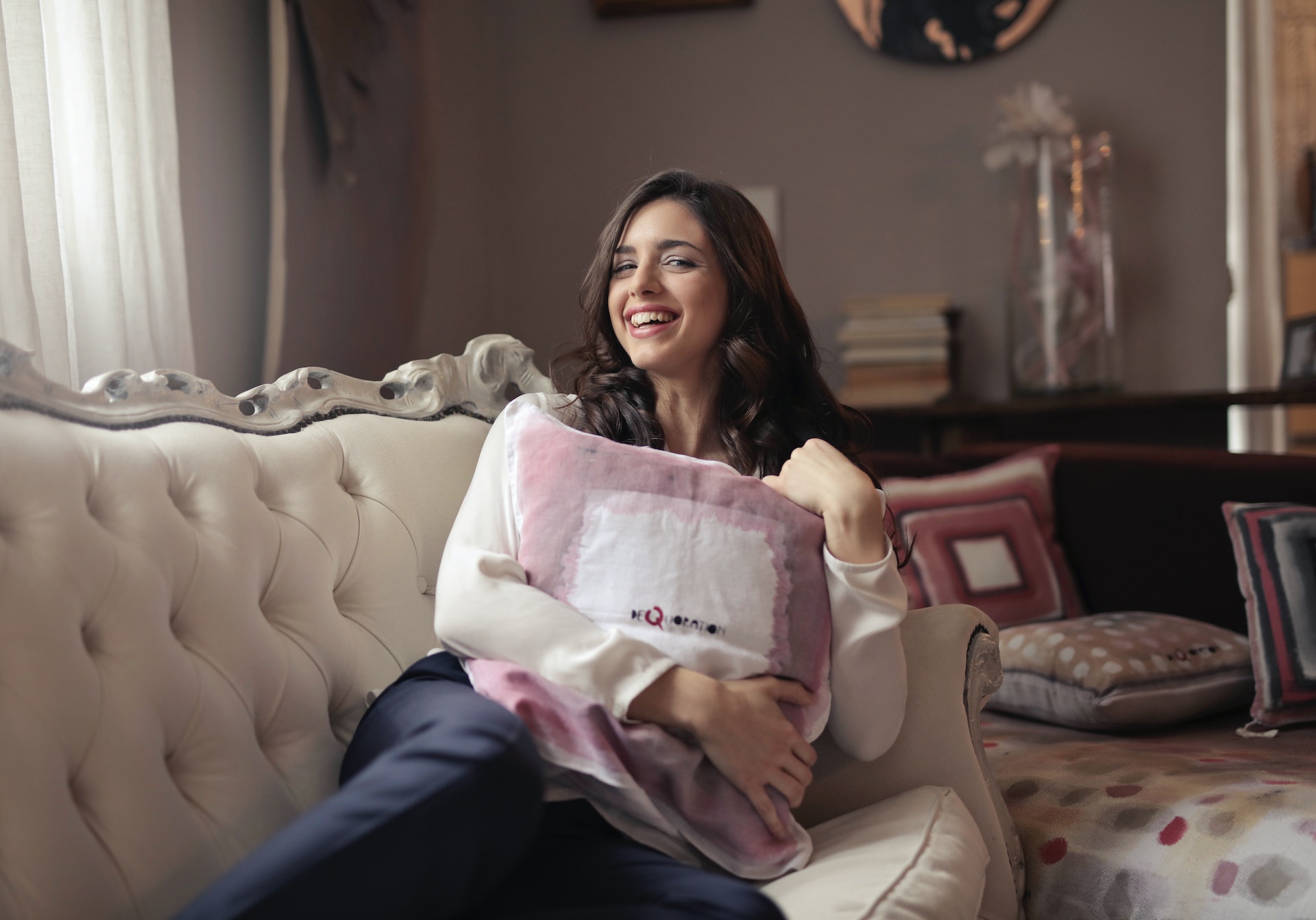Woman sitting on a couch in her apartment, smiling, in white top