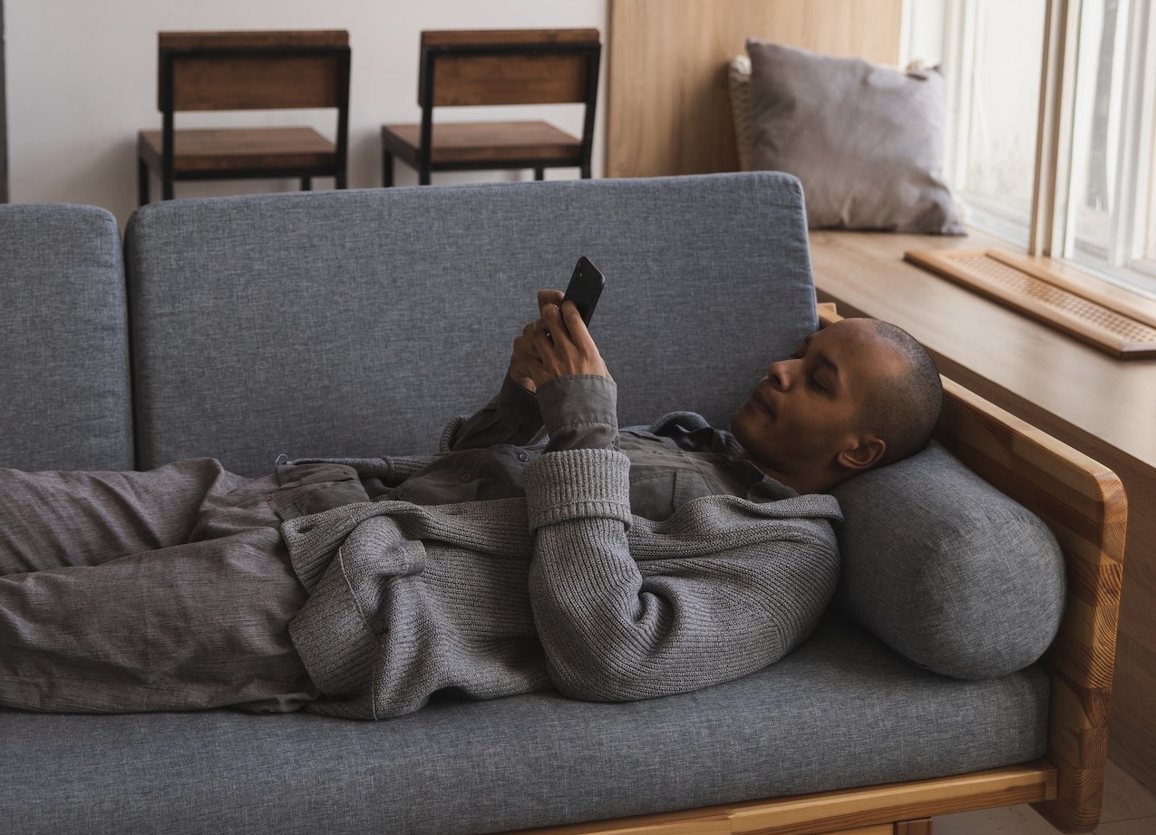 Man is laying on the bed and texting on his phone.