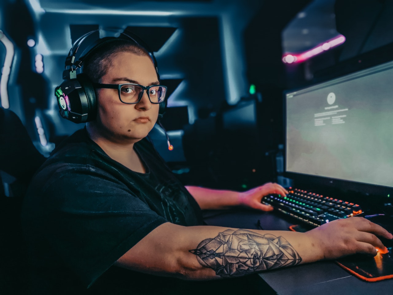 Woman with tattoo wearing headphones and glasses is playing a game.